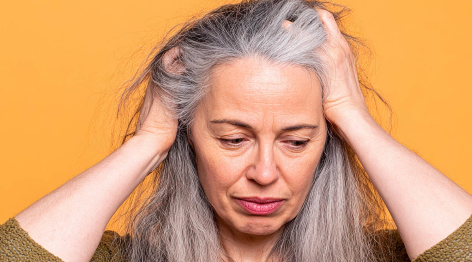 Woman with long gray hair holding her head in frustration against an orange background