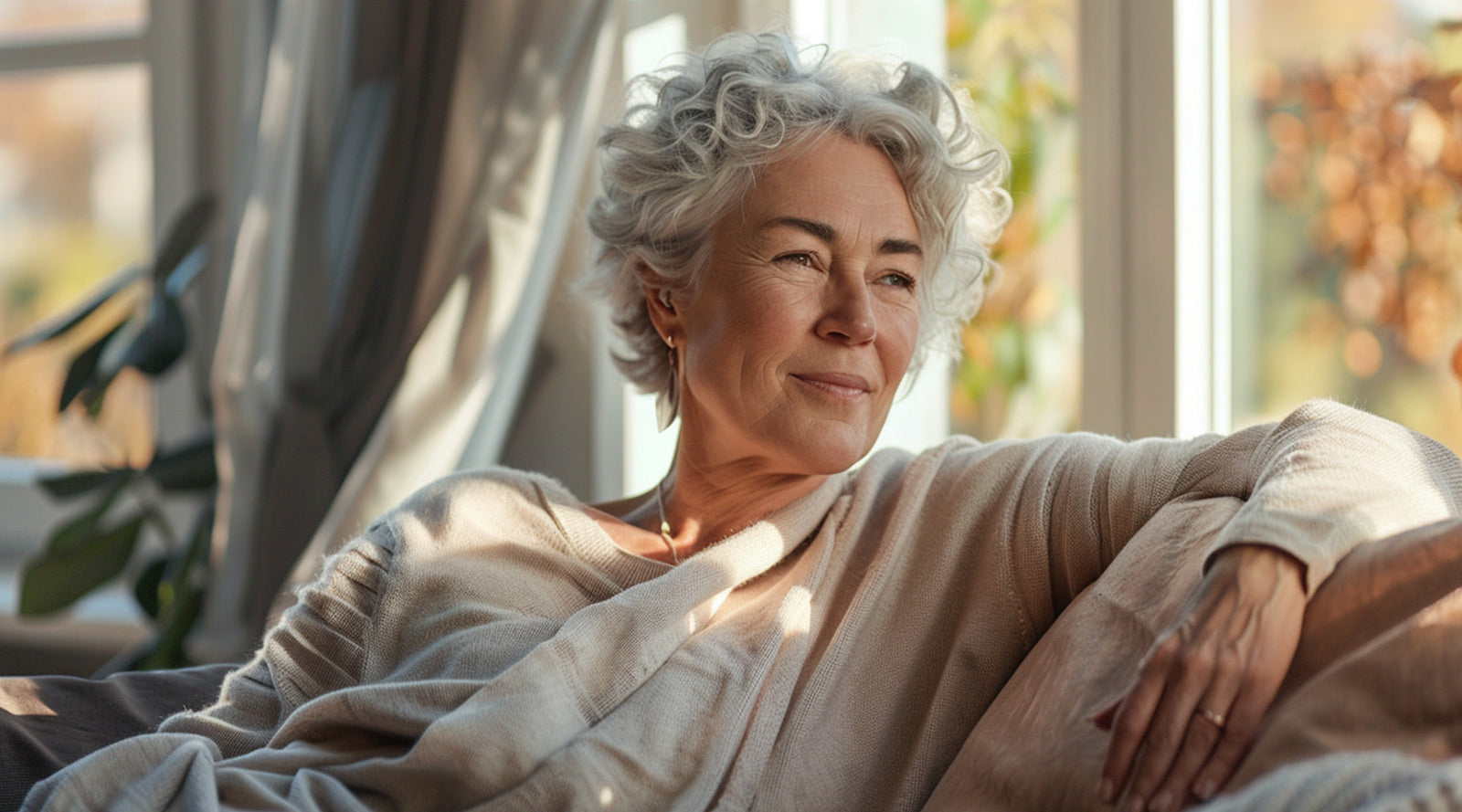 Woman with short, curly gray hair relaxing on a couch in natural light