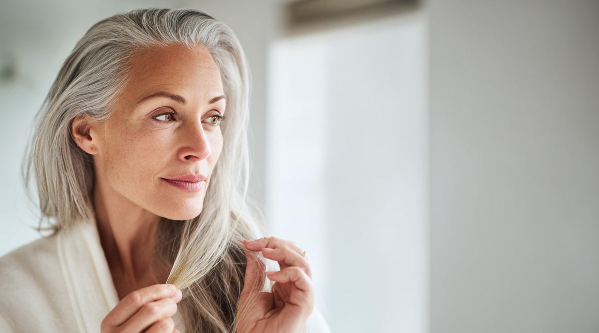 Woman with long gray hair examining a strand