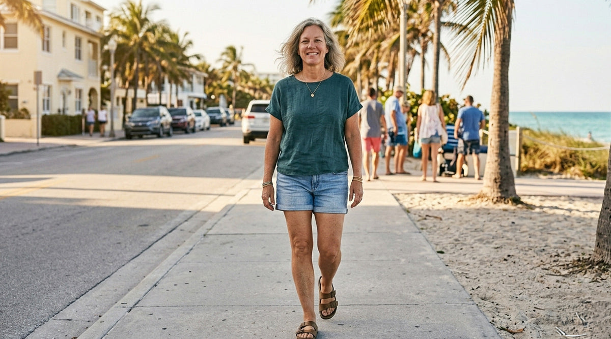Smiling woman with gray hair walking outdoors on a sunny street with palm trees