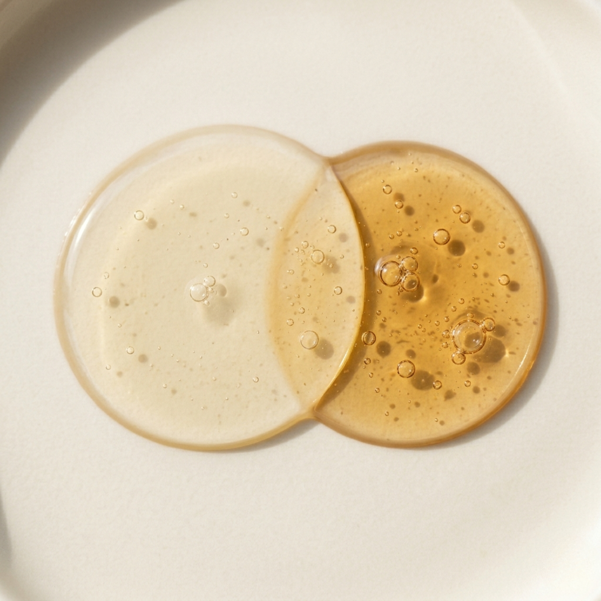 Two droplets of liquid, one beige and one brown, on a light background.