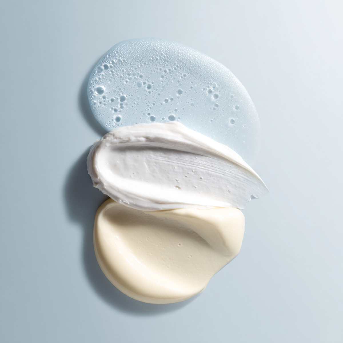 There swatches of gray hair care products on a light blue background